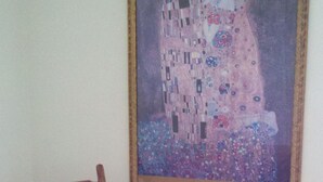 Een houten stoel met een rode kussens op een kamer met een schilderij in een lijst aan de muur.
