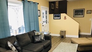 A living room with a dark brown sofa, a light-colored coffee table, and a beige ottoman. There is a staircase with a trash can and framed pictures on the wall. - Stay Where The Stars Stay! And we think everyone who stays with us is a STAR! (Nashville)