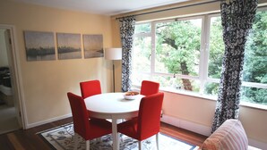 A dining area with a round table, red chairs, a bowl of fruit, and a window with curtains. - Beautiful 2 Bedroom Private Apartment (London)