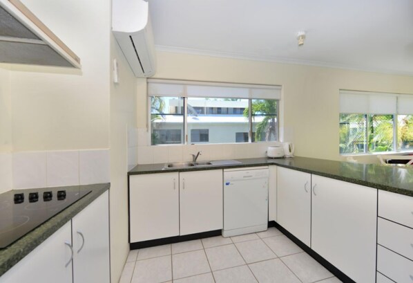 A modern kitchen with white cabinets, a black countertop, a dishwasher, and a window with a view of buildings and trees.