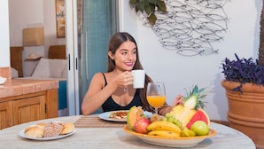 Una persona seduta a tavola con prodotti per la colazione, tra cui croissant, frutta e un bicchiere di succo d'arancia.