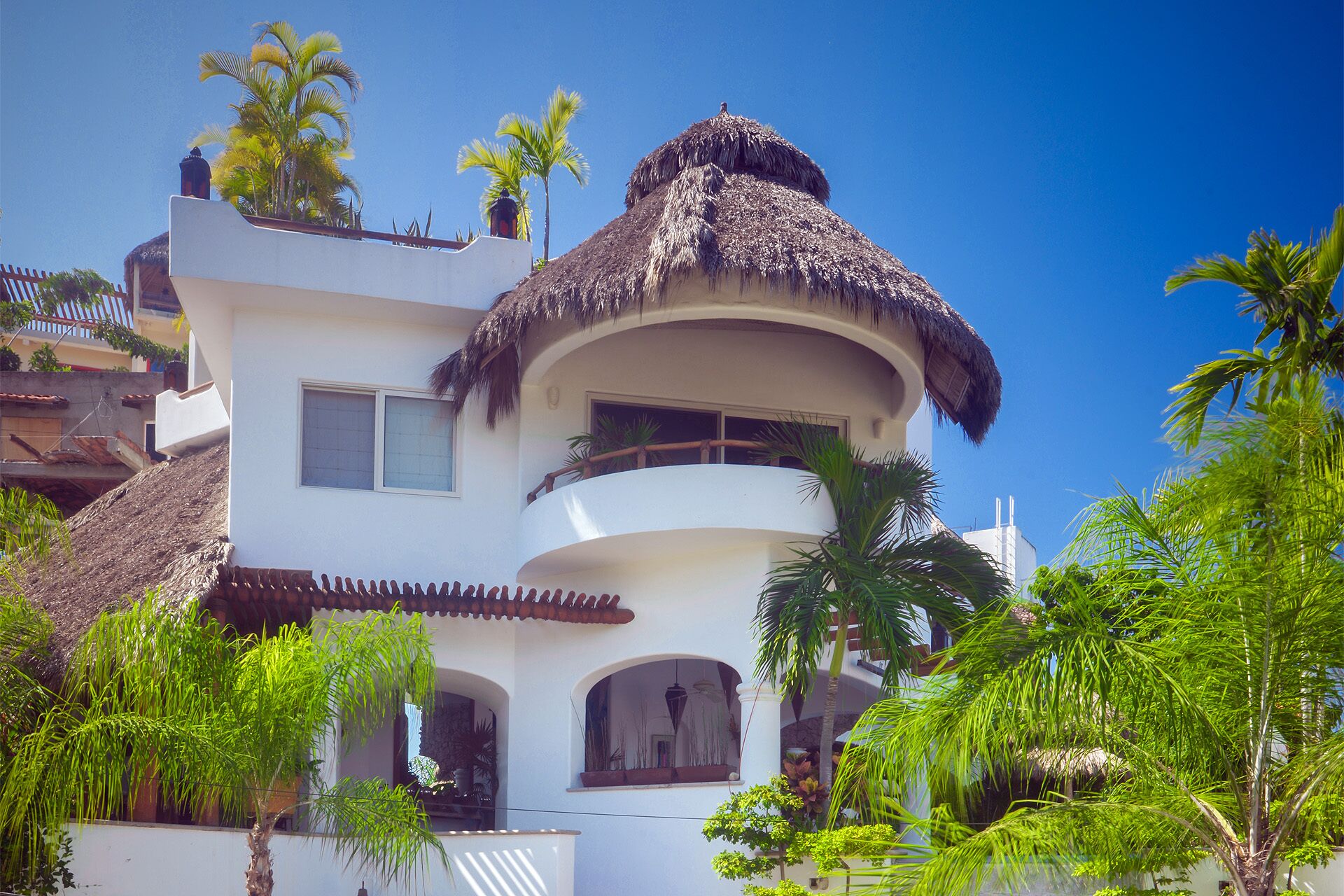 Un edificio blanco con techo de paja, varios balcones y palmeras alrededor.