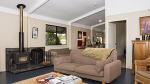 A living room with a fireplace, a sofa, a coffee table with books, and a dining area in the background.