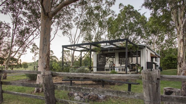 A rustic wooden structure with a metal roof, surrounded by a wooden fence, set in a grassy area with trees. - Gatekeepers' cabin (Boonah)