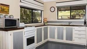 A kitchen with a microwave, stove, and sink. There is a clock on the wall and a window with a view of cows.