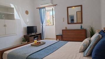 Un dormitorio con cama, tocador, televisor, ventana con cortinas y espejo en la pared.