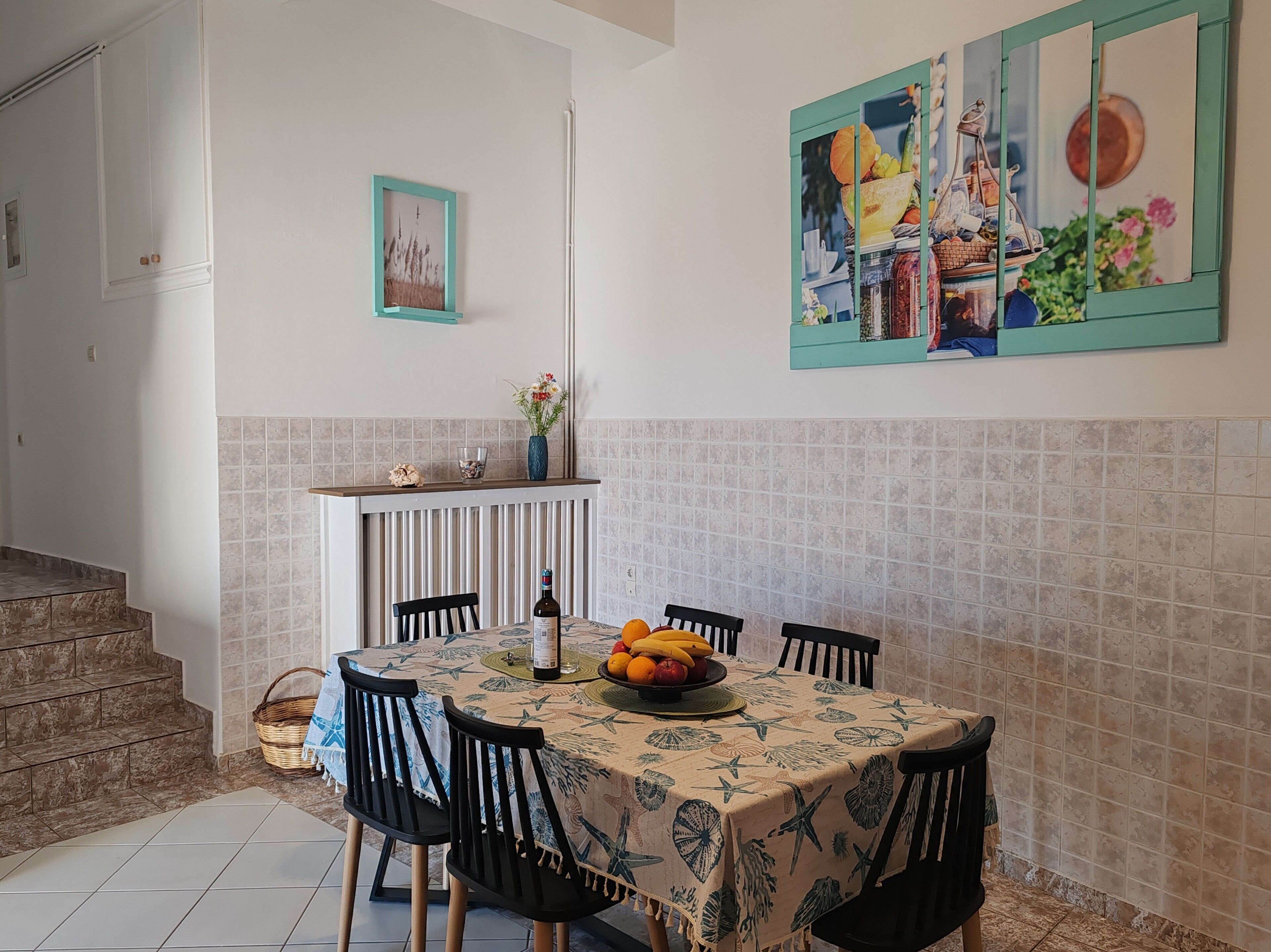 Un comedor con una mesa dispuesta para cuatro personas, rodeada de sillas. En la mesa, un jarrón con flores y un frutero.