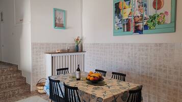 Un comedor con una mesa dispuesta para cuatro personas, rodeada de sillas. En la mesa, un jarrón con flores y un frutero.