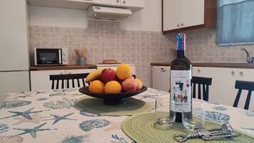 Uma cozinha com uma mesa posta para refeições, apresentando uma garrafa de vinho NICO LAZARDI, uma tigela de frutas e um abridor de garrafa.