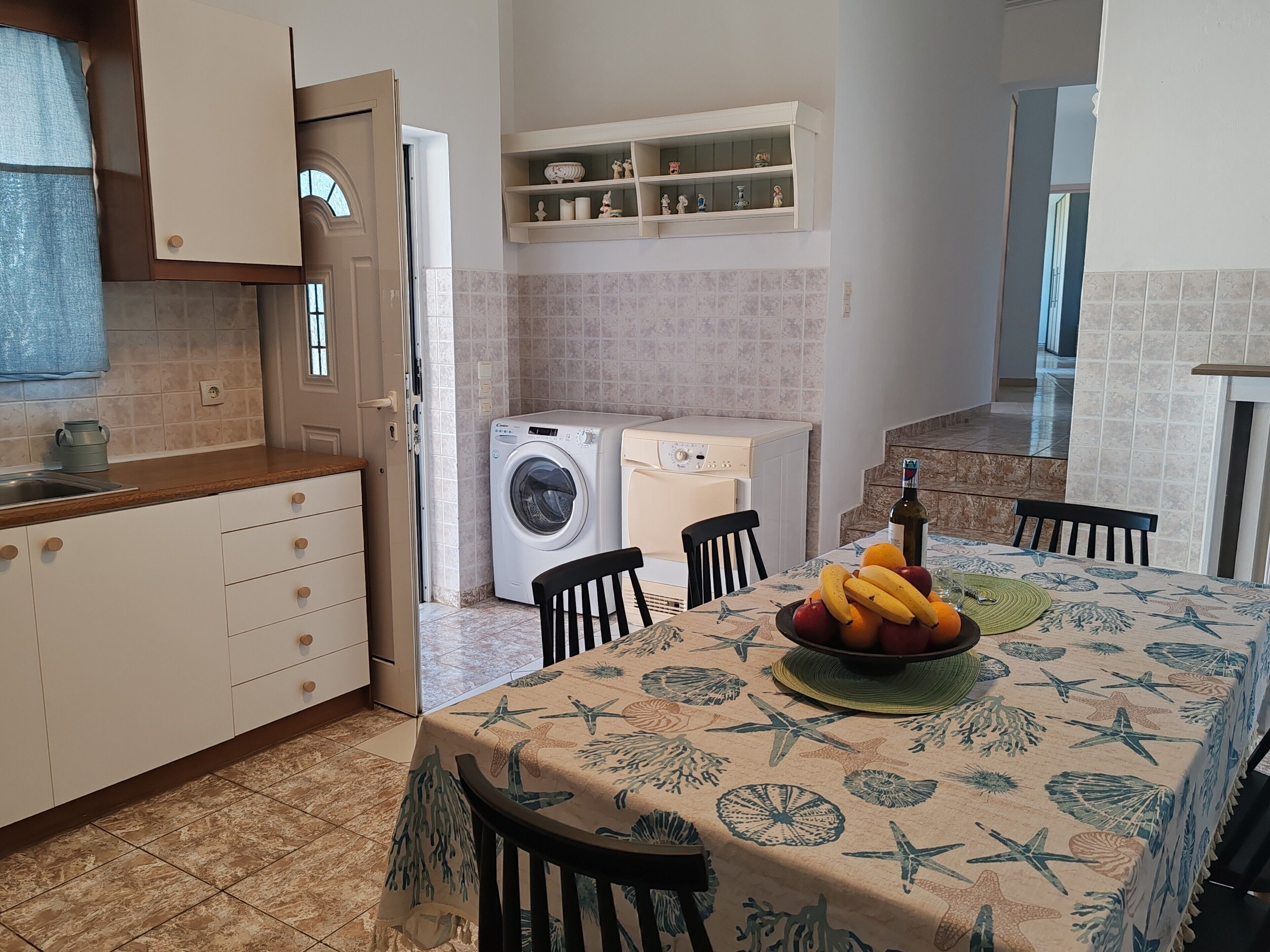 A compact kitchen with a washing machine, a dining area with a table set for two, and a small shelf with decorative items.