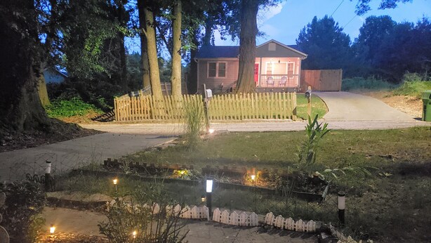Een woonwijk met een huis, een houten schutting en een tuin met kleine lichtjes.