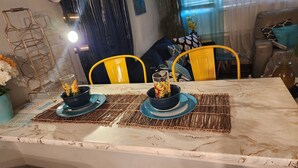Een eetgedeelte met een marmeren aanrecht, twee blauwe kommen met zonnebloemen, gele stoelen en een decoratieve metalen rek.