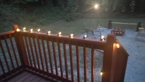 Een houten terras met leuningen en sfeerverlichting.