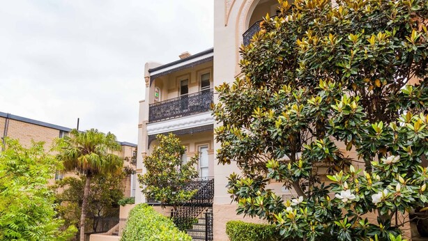A building with a checkered pathway leading to a gated entrance, surrounded by lush greenery and a well-maintained garden. - Quiet Glebe Studio Near Parks & Cafés (Glebe)