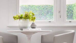 A room with a white round table, two grey chairs, a white vase with green plants, and a window with a view of greenery outside. - Quiet Glebe Studio Near Parks & Cafés (Glebe)