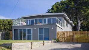 A modern two-story house with large windows, a balcony, and a fenced yard.