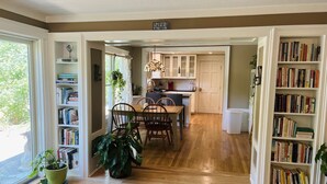 A spacious kitchen with wooden flooring, a dining area with chairs, and a bookshelf filled with books.