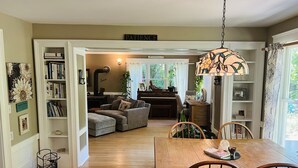 A cozy living room with a piano, a dining table with chairs, and a bookshelf filled with books.