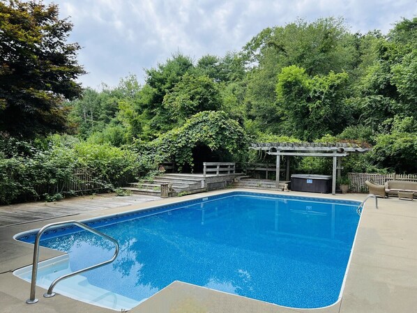 Piscina rectangular con cubierta de madera y pérgola en un entorno natural exuberante y verde.