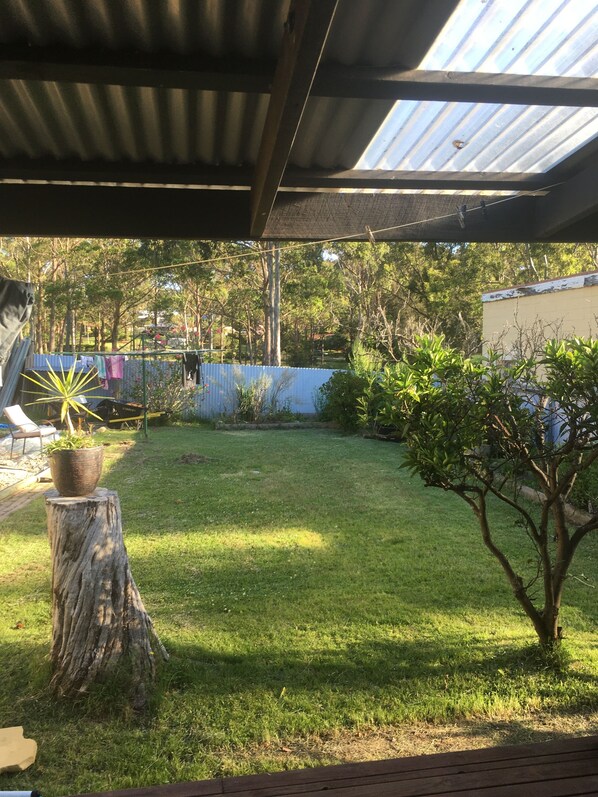 A covered outdoor area with a grassy lawn, a wooden stump with a potted plant, and a small tree. - hillview@batemans bay (Batemans Bay)