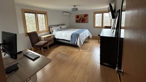 Une chambre à coucher avec un lit, un bureau avec un ordinateur, une chaise et deux fenêtres.