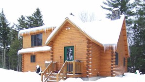 A log cabin with a wooden exterior, a front porch, and a staircase leading to the entrance.