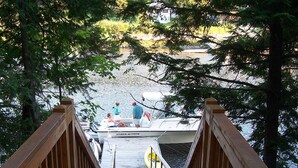 A wooden dock leading to a boat with people on it, surrounded by trees and water.