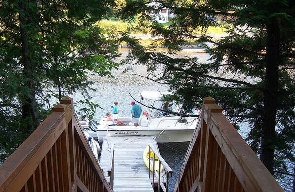 A wooden dock leading to a boat with people on it, surrounded by trees and water.