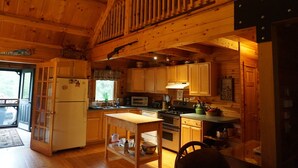 A wooden cabin interior with a kitchen, dining area, and a balcony.