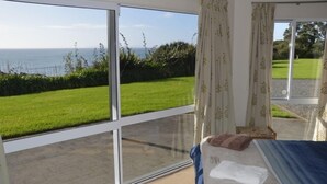 A bedroom with a large window overlooking a grassy area and the sea.