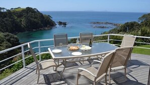 A deck with a table and chairs overlooking a coastal view.