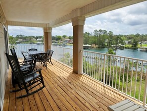 Um deck de madeira com mesa e cadeiras, com vista para um lago com barcos e casas.