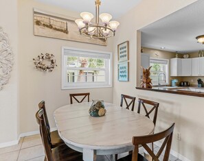 Un coin repas avec une table ronde, des chaises en bois, un lustre et une vue sur l’extérieur par une fenêtre.