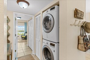 A laundry area with stacked washers and dryers, a mirror, and a wall-mounted rack with bags. - Path to relaxation! (Indian Rocks Beach)