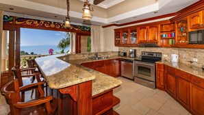 A kitchen with a large island, wooden cabinets, granite countertops, and a view of the ocean.