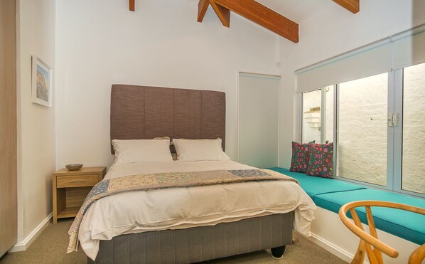A bedroom with a bed, bedside table, and a window seat with cushions.