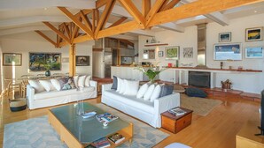 A spacious living area with high ceilings and exposed wooden beams, featuring a white sofa set, a glass coffee table, and a fireplace. - Breathtaking Clifton 4th beach villa (Clifton)