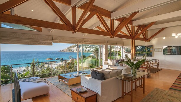 A spacious living area with a large window overlooking a beach and ocean. There is a sofa, a coffee table, and a TV. - Breathtaking Clifton 4th beach villa (Clifton)