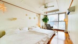 Une chambre avec un grand lit, un ventilateur de plafond, une fenêtre avec des stores et une plante en pot.
