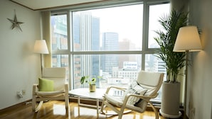 Un salon moderne doté d’une grande fenêtre, de deux fauteuils à bascule, d’une petite table avec une plante et d’une plante en pot placée près de la fenêtre.