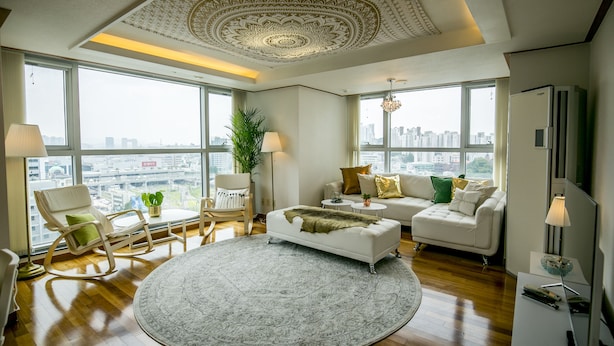 Un salon spacieux agrémenté d’un grand tapis rond, d’un canapé blanc, d’un fauteuil blanc et d’une table à manger avec des chaises.