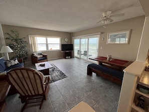 Relax in this spacious living area with a high ceiling, ceiling fan, and ocean views from the large window.
