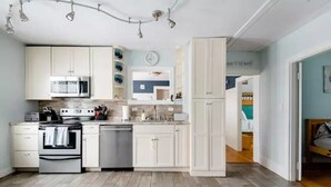 A modern kitchen with white cabinets, stainless steel appliances, and a wooden floor. - Adorable Beach House Across the Street From Beach! (Scarborough)