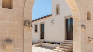 A stone archway leading to a building with a white facade, a small window with flowers, and a door. - Trappeto Dellago with pool, parking & wi.fi  (Avola-Noto (siracusa))