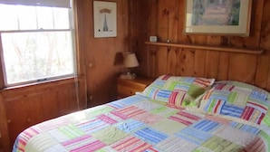 Une pièce de style cabane en bois, avec un lit, une table de chevet, une lampe, un tableau encadré au mur et une fenêtre.