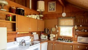 Une cuisine de taille réduite, dotée de meubles de rangement en bois, d’une cuisinière, d’un four à micro-ondes et d’un évier.