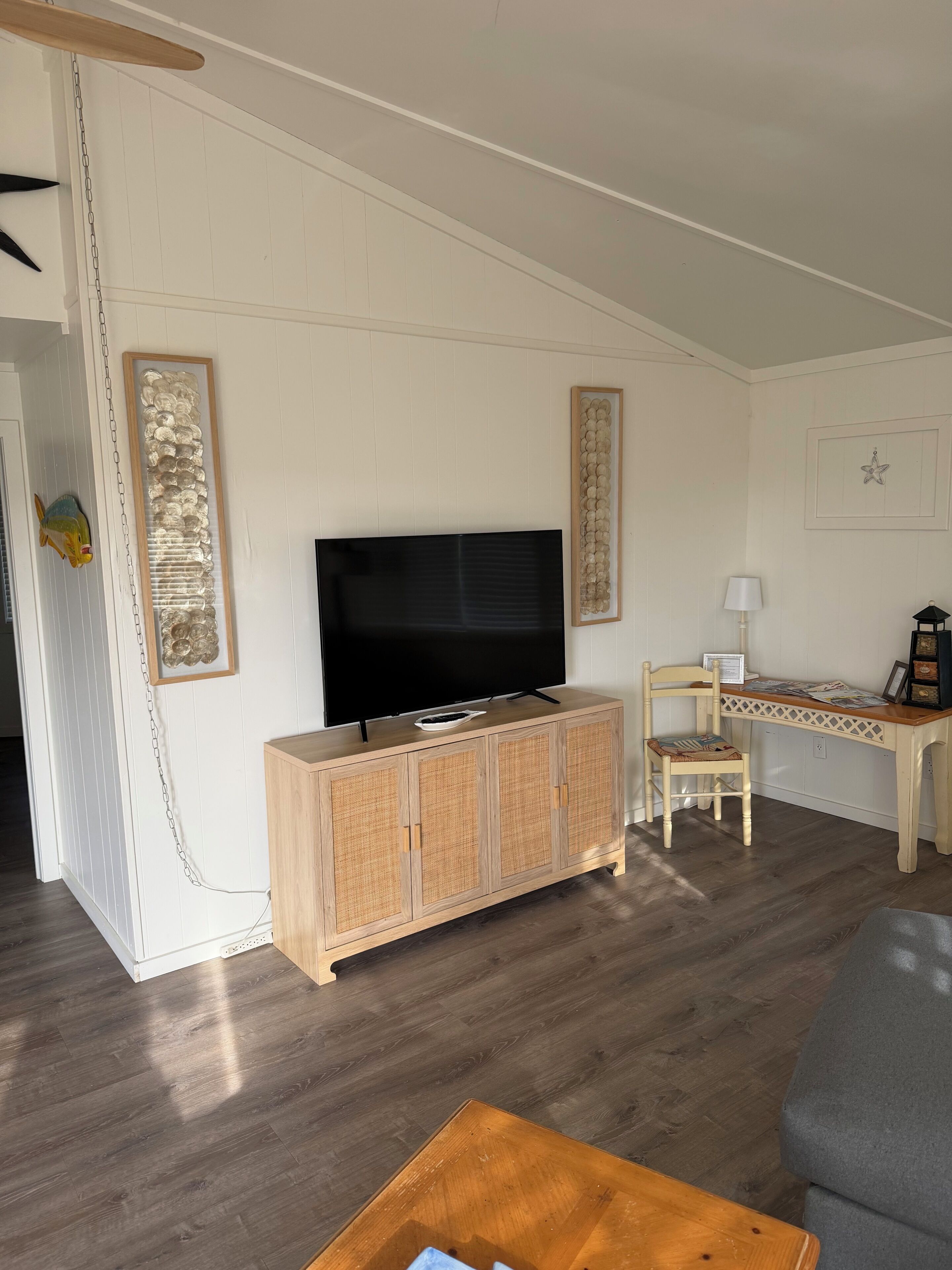 A living room with a flat-screen TV on a wooden cabinet, a dining area with a table and chairs, and a wall-mounted star decoration.