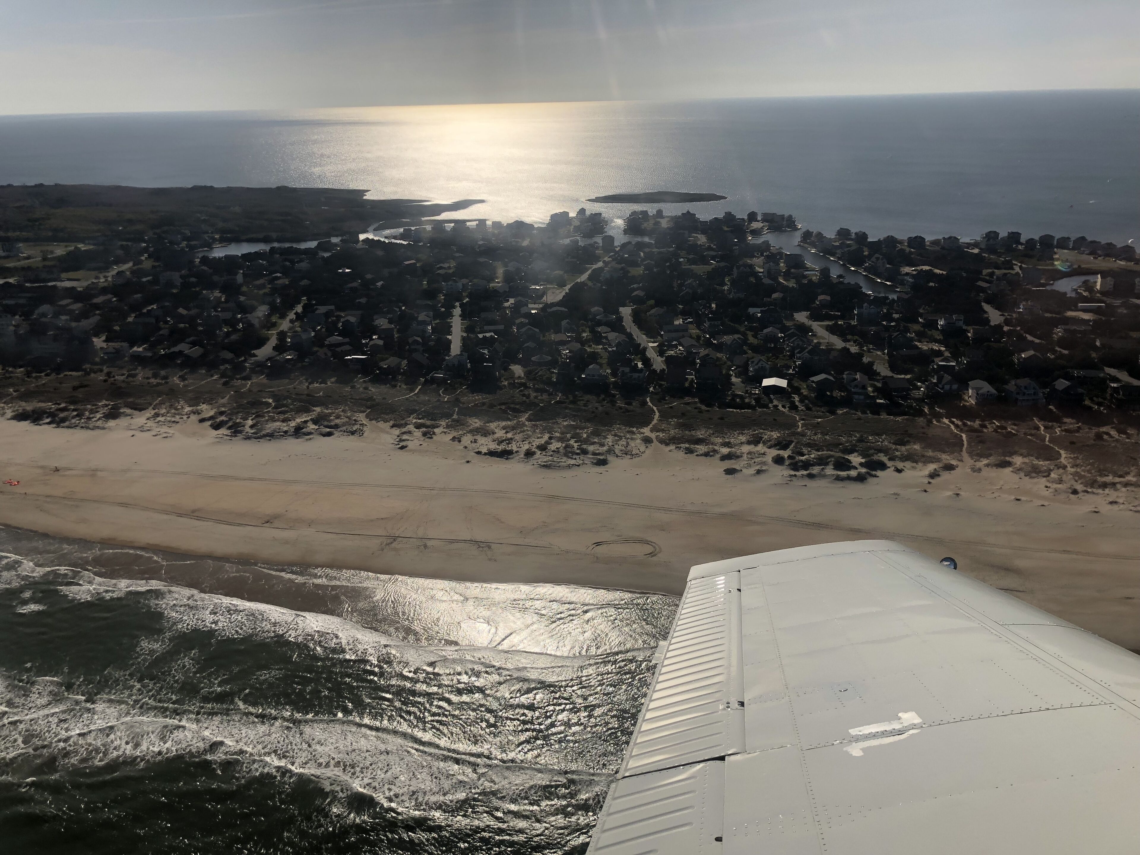 Vista aerea di una zona costiera con spiaggia, una piccola isola e una cittadina densamente popolata.