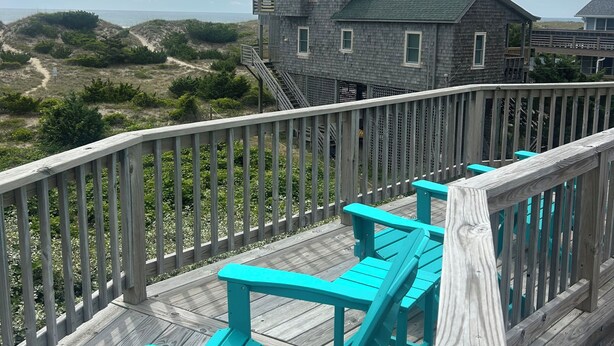 Una terraza de madera con bancos turquesa, una casa con techo verde y vistas a la playa.