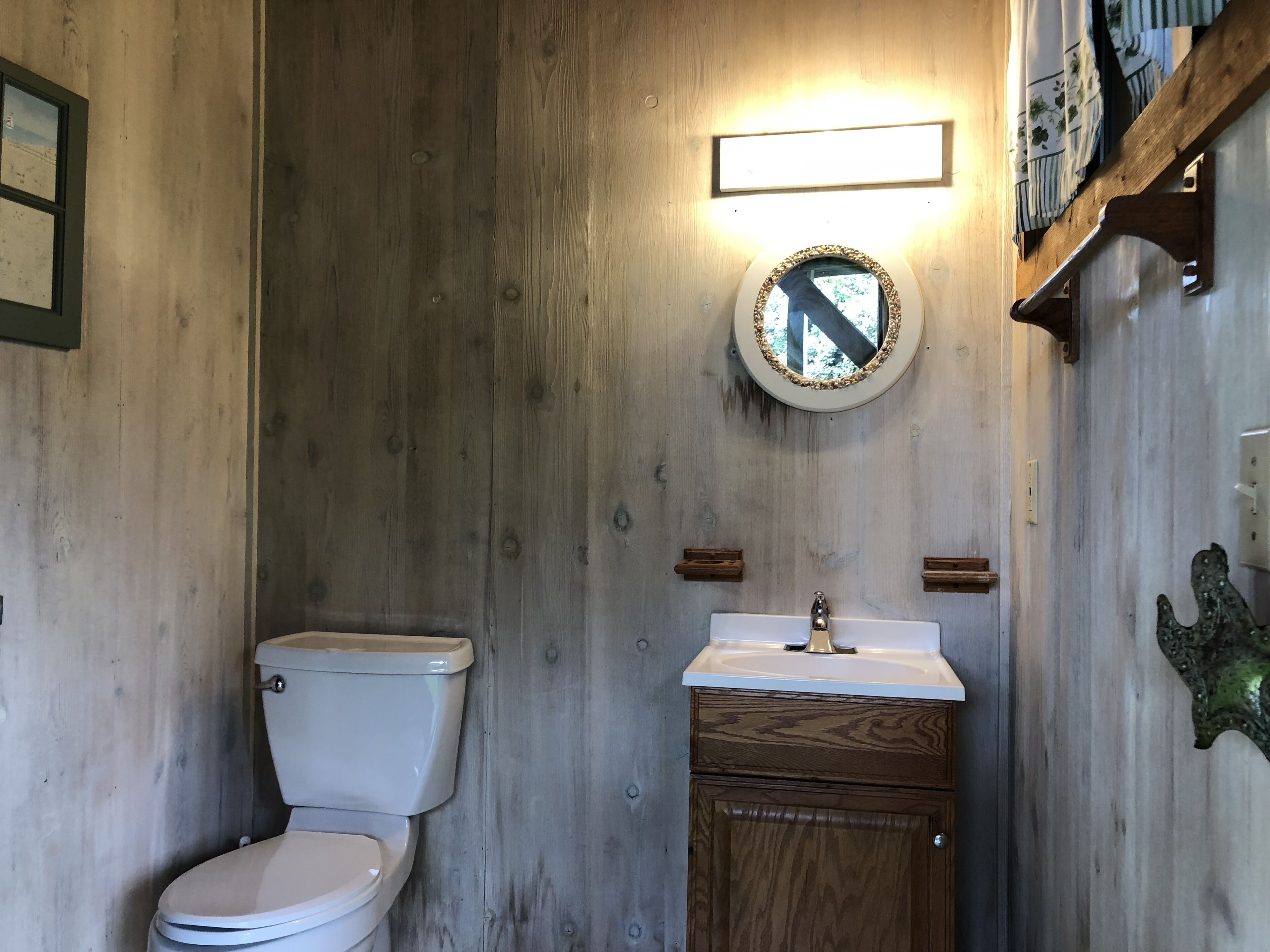 A bathroom with a wooden wall, a toilet, a sink with a mirror, and a shelf with a decorative item.